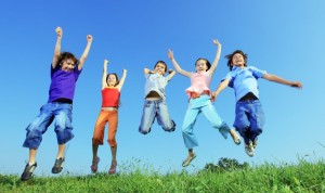 Group of five happy children jumping outdoors.